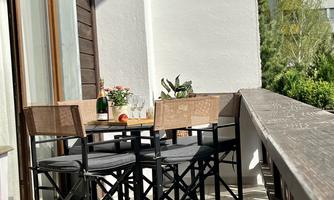 A cozy balcony with two chairs and a table. On the table are plants and a glass of water, surrounded by a beautiful view.