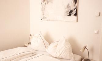 A cozy bedroom with a double bed and white bed linens. A modern black-and-white painting hangs on the wall.