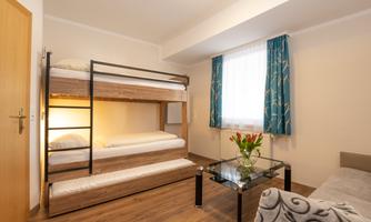 A modern room with a bunk bed and bright light. There is a small table with a vase full of flowers and colorful curtains.