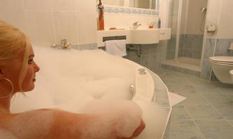 A person is relaxing in a bathtub full of foam. The room is bright and modernly designed.