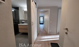 A bright hallway with modern furniture and a bathroom in the background. The floor is light, and the space feels inviting.