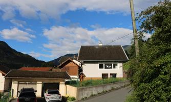 A quiet residential area with a white house and a view of the mountains. The sky is blue with some clouds.