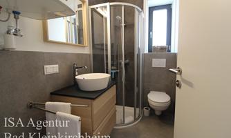A modern bathroom with a shower, a sink, and a toilet. The walls are in neutral colors and there is a large mirror.