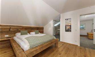 A cozy bedroom with a large wooden bed and minimalist furnishings. The warm wood tones and soft light create a relaxed atmosphere.