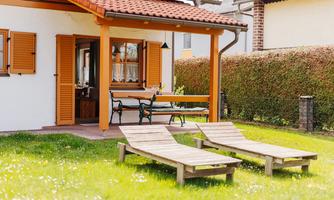 A cozy house with a covered terrace and two loungers in the garden. The surroundings are green with a well-maintained garden.