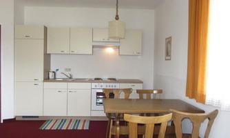 A bright and cozy kitchen with modern furniture. A wooden chair dining table and a large window with an orange curtain create an inviting atmosphere.