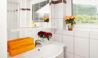 A bright bathroom with a sink and a fresh floral arrangement. Orange towels are neatly placed next to the sink.