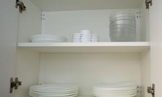 An open cabinet with white plates and glasses. The utensils are neatly arranged and well visible.