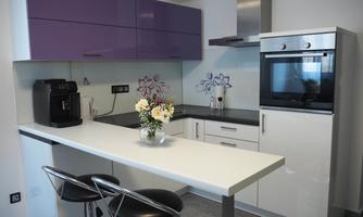 A modern kitchen with purple cabinets and a stainless steel countertop. There is a breakfast bar with stools and fresh flowers on the table.