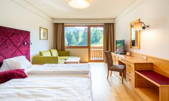 A modern hotel room with two beds and a large window. The room has a bright, cozy decor and a view of the mountains.