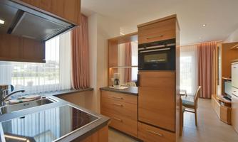 A modern kitchen with wooden cabinets and stainless steel appliances. Plenty of light comes through the windows, creating an inviting atmosphere.