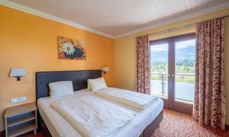 A bright hotel room with two single beds and a balcony. The walls are orange, and large windows offer a view of the countryside.
