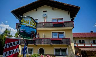 A charming guesthouse with a balcony and an inviting sign. In the foreground is a "Room Available" sign and colorful flowers are blooming.