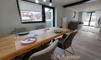 A modern dining area with a large wooden table and stylish chairs. Plenty of daylight streams through the windows, creating an inviting atmosphere.