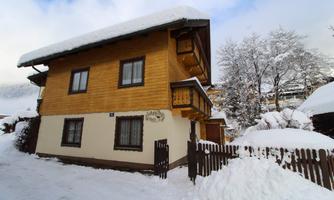 A cozy wooden house in the snow with a snow-covered roof. Surrounded by a winter landscape and trees.