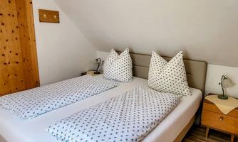 A cozy bedroom with a double bed and two large pillows. The walls are light, and there is a wooden wardrobe as well as nightstands.
