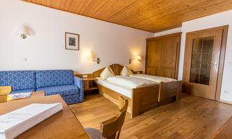 A comfortable room with a double bed and a blue sofa. The wooden ceiling and floor give the space a cozy atmosphere.