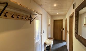 A bright hallway with wood details and a shoe rack. Coat hooks are hanging on the wall and there are several doors.
