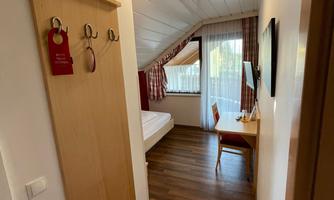 A cozy hotel room corridor with a wooden coat rack and a table. Daylight is shining through the window, and the walls are designed in light colors.