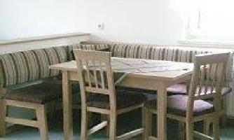 A simple dining area with a wooden table and chairs. The seating consists of a padded bench and has a simple decor.