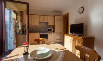 A bright kitchen with wooden cabinets and a table. A television and a microwave are visible in the room.