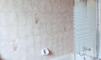A simple bathroom with a bathtub and a shower partition. The walls are decorated with beige tiled tiles.