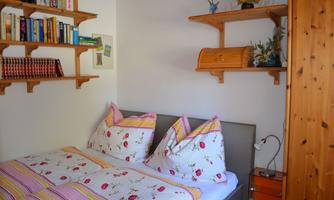A cozy bedroom with a double bed and colorful pillows. Wall-mounted bookshelves and decorative elements are present.