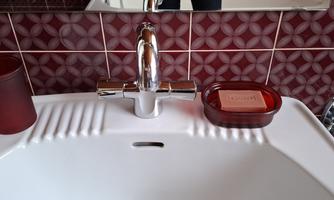A modern sink with a shiny faucet and a red soap dispenser. In the background, there are red tiles with a geometric pattern.
