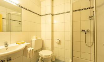 A modern bathroom with white tiles and a shower. There is a sink and some towels.