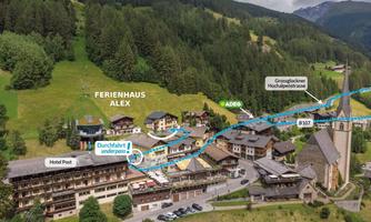 An aerial view of a picturesque village with several buildings, including the holiday home Alex and the Hotel Post. Surrounded by green hills and mountains, the map also shows important transportation routes.