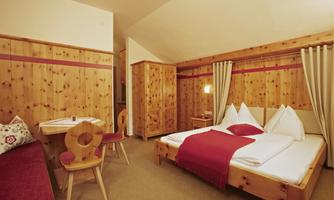 A cozy bedroom with wooden walls and cheerful accents. There is a double bed, a seating area, and a table.