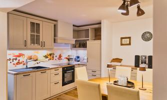 A modern kitchen with bright furniture and a wooden floor. The dining area is cozy with a round table and chairs.