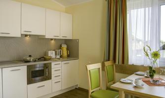 A modern kitchen with white cabinets and stainless steel appliances. On the table, there are tea cups and a small flower vase.