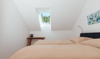 A cozy bedroom with two beds and a skylight. The room is bright and furnished in a modern style.