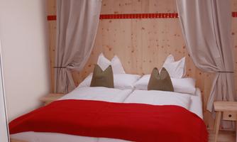 A cozy bedroom with a large bed and white bed linens. The walls and furniture are made of light wood, and red and gray accents create an inviting atmosphere.