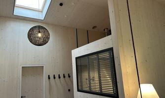 A modern interior with wood paneling and a large window. A decorative lamp hangs from the ceiling, and there is a gray wall with blinds.