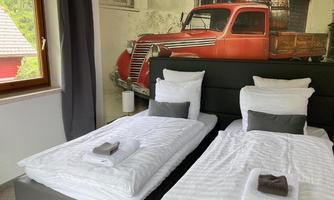 A cozy bedroom with two single beds and freshly laundered bedding. In the background, there is a mural of an old red truck.