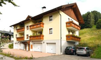 A modern apartment building with brown balconies and a bright facade. It is situated in a rural setting with a parking lot for cars.