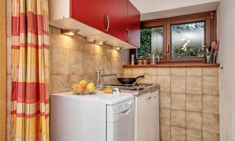 A small kitchen with red cabinets and modern appliances. A window with a view of the outdoors and colorful curtains complement the space.