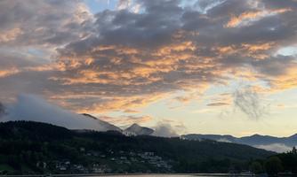 A picturesque landscape by the lake with mountains in the background. The sky is adorned with colorful clouds at sunset.