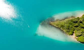 A picturesque lagoon with clear turquoise water and green vegetation. A small boat can be seen in the water.