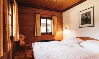 A cozy bedroom with a double bed and wooden paneling. Large windows provide plenty of natural light.