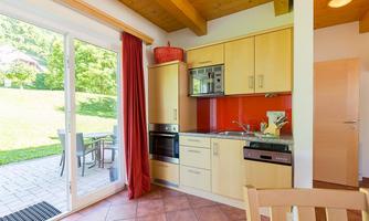A modern kitchen with bright furniture and red accents. It has large windows that let in light and provide a view of the outside area.