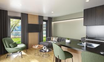A modern living kitchen with a cozy sofa and a table. Large windows provide a beautiful view of the outdoors.
