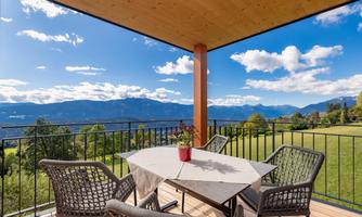 A beautiful balcony with a round table and chairs. In the background, the mountains and the blue sky with white clouds can be seen.