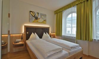 A modern bedroom with two single beds and a wooden frame. The walls are bright and decorated with green curtains, while a piece of art hangs on the wall.