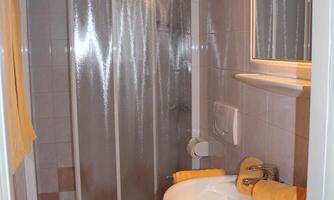 A small bathroom with a shower cubicle and a sink. The walls are light tiled and there is a mirror above the sink.