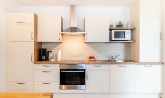 A modern kitchen with white cabinets and a wooden countertop. The amenities include a stove, a refrigerator, and a microwave.