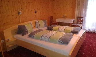 A cozy bedroom with a large bed and bright pillows. The walls are paneled with wood and there is a table as well as chairs in the room.