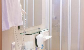 A modern bathroom with a sink, a mirror, and a shower. The walls are light, and there are towels and hygiene products.